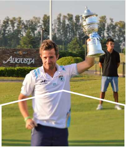 A man holding a championship cup with another man and trees in the background.